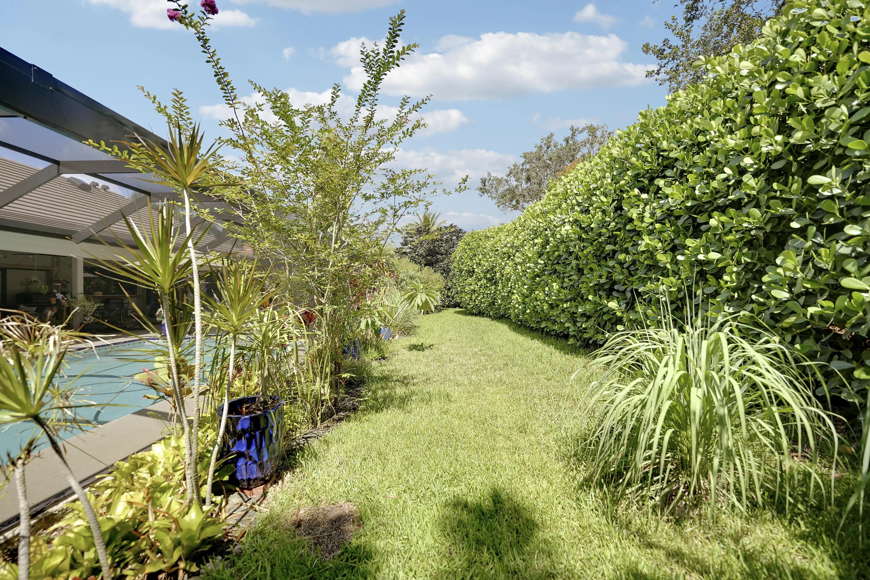 landscaped area behind the pool offers a private, serene greenway bordered by mature hedges. It provides a peaceful backdrop to the outdoor living space and enhances the home’s overall privacy.