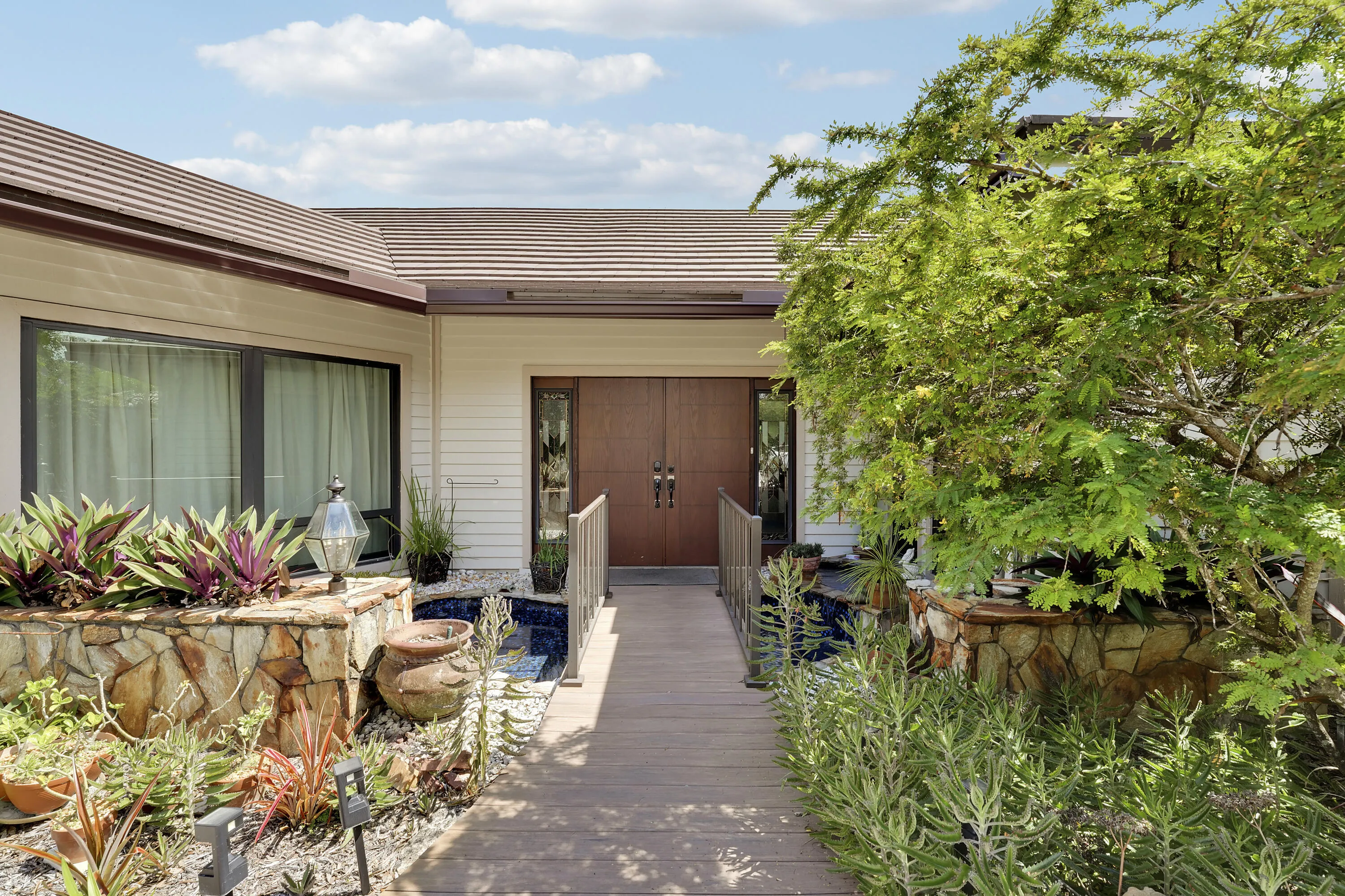 A beautiful front double door entrance featuring a bridge walkway over a serene cascading water feature