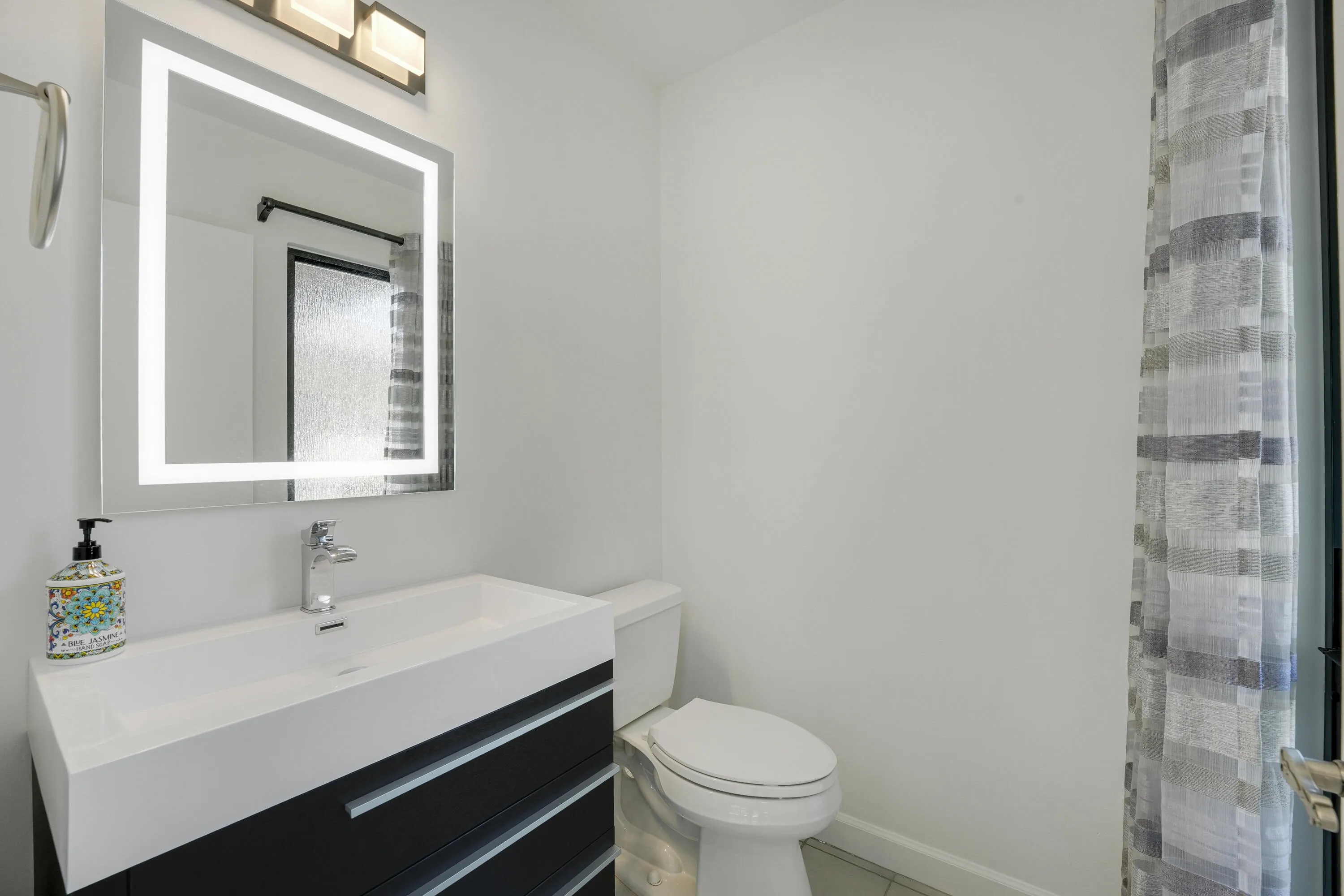 Remodeled half bath off the greatroom featuring a sleek modern vanity, LEDlit mirror, updated fixtures, and fresh contemporary finishes