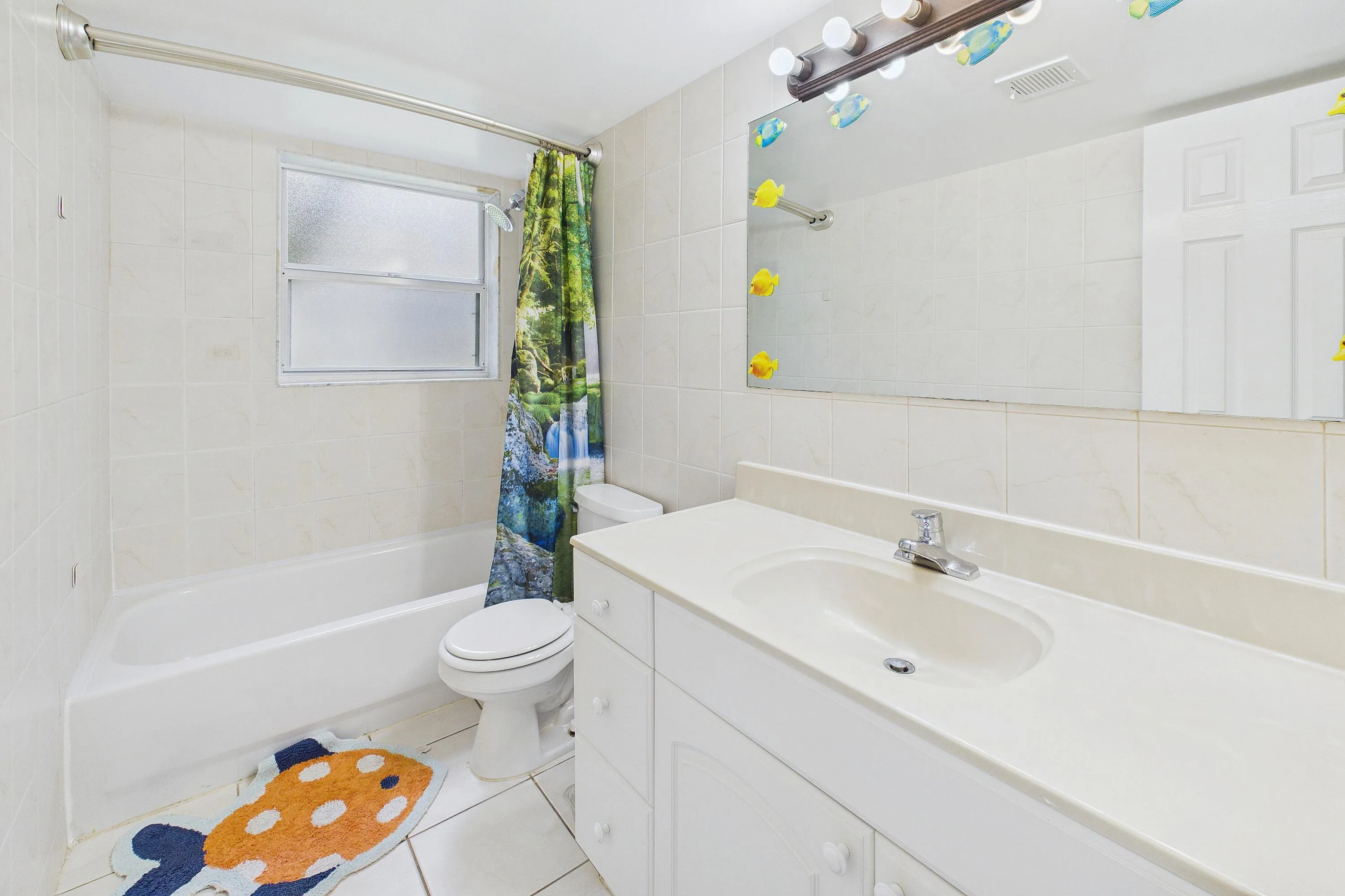 Bathroom featuring a white vanity with integrated sink, chrome faucet, wall-mounted mirror, and a white bathtub with tile surround