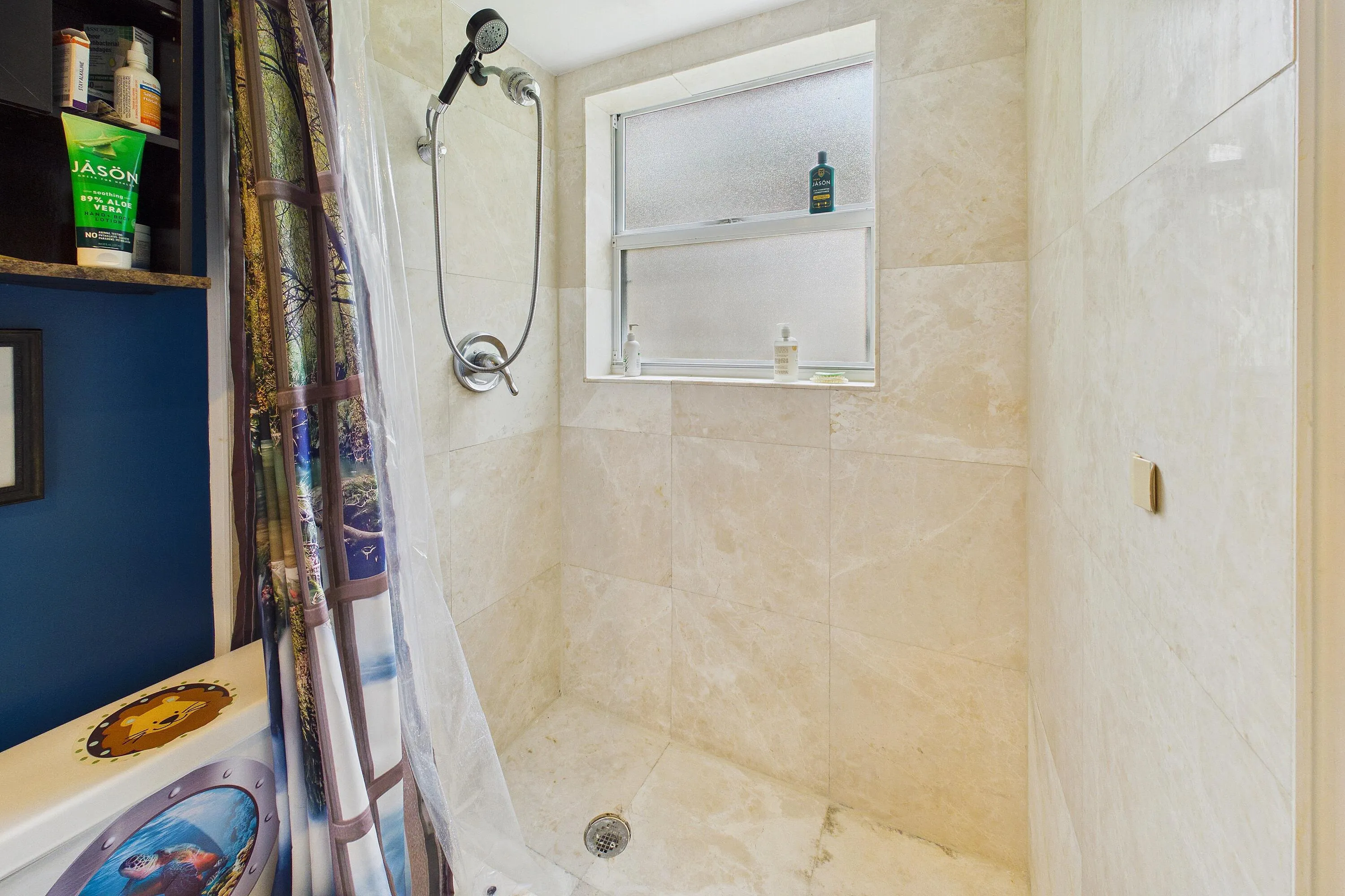 Tiled shower enclosure with a fixed pane window, chrome shower fixtures, and integrated wall shelving
