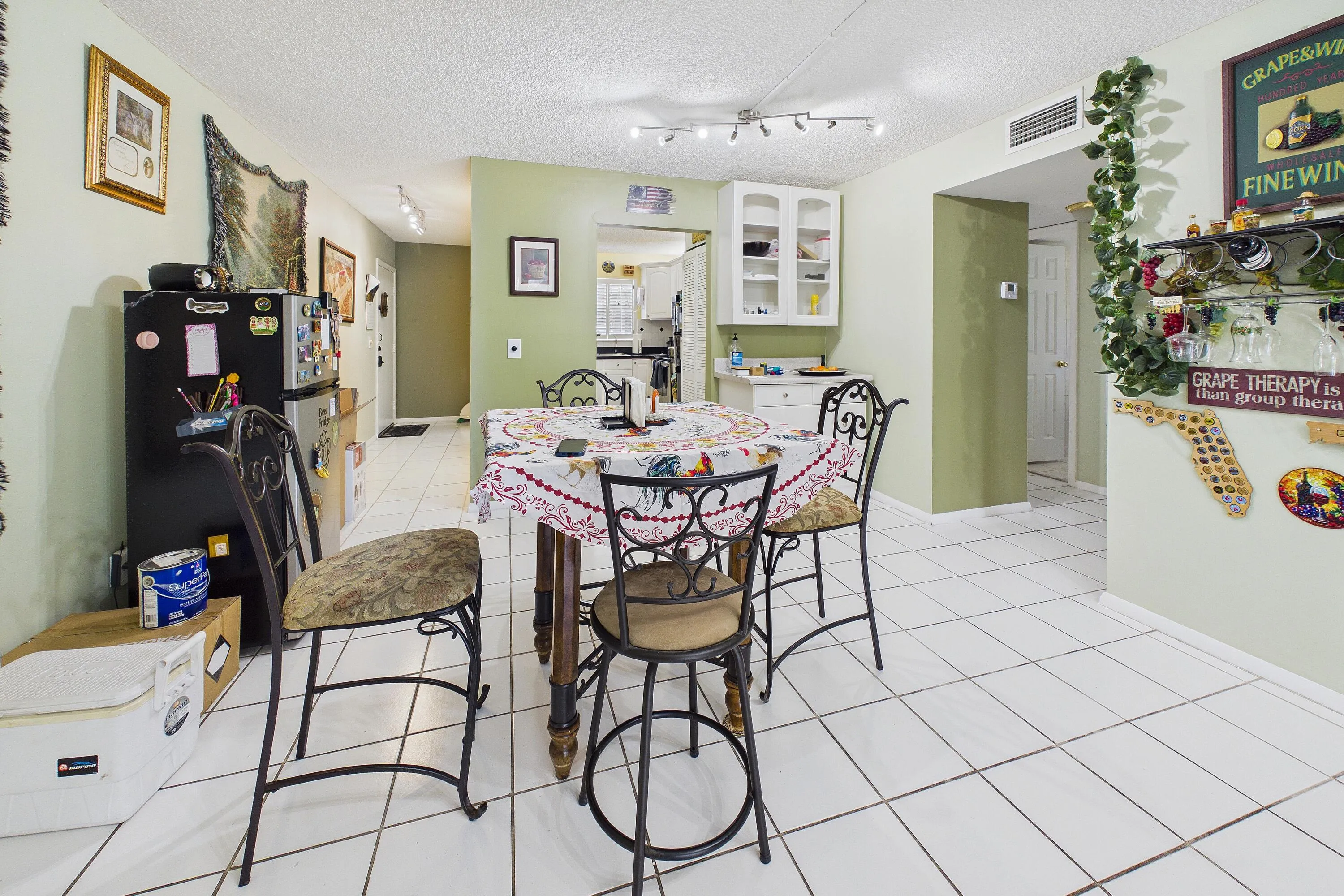 White tile flooring throughout, track lighting, and a partial kitchen with white cabinetry