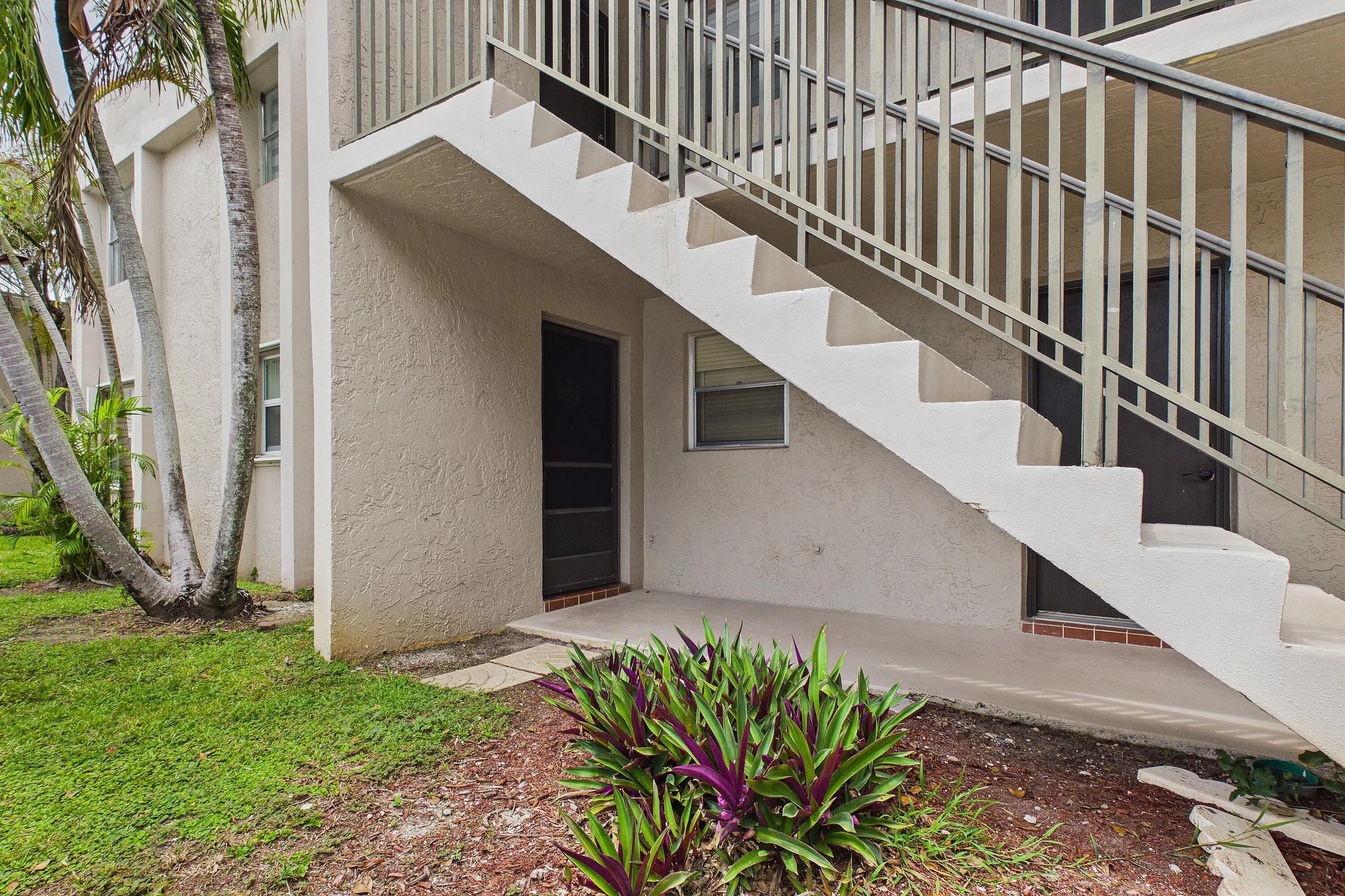 Exterior stairs with metal railings, stucco facade, and established landscaping