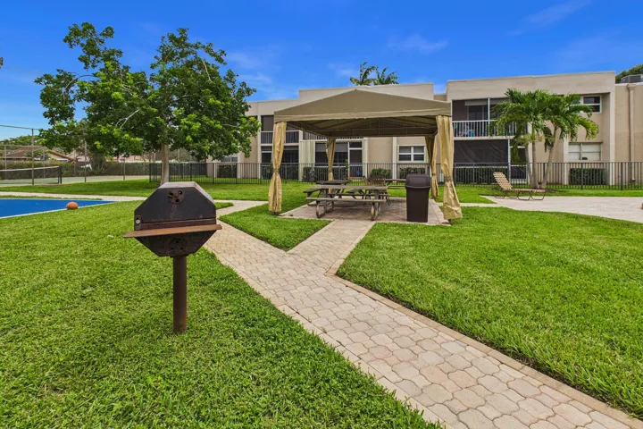 Expansive green space featuring a paved pathway, covered outdoor seating area, and a barbecue grill