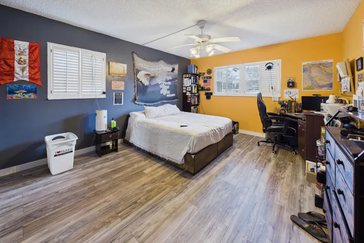 Wood-finish flooring throughout, multiple windows with white louvered shutters, and a ceiling fan with integrated lighting