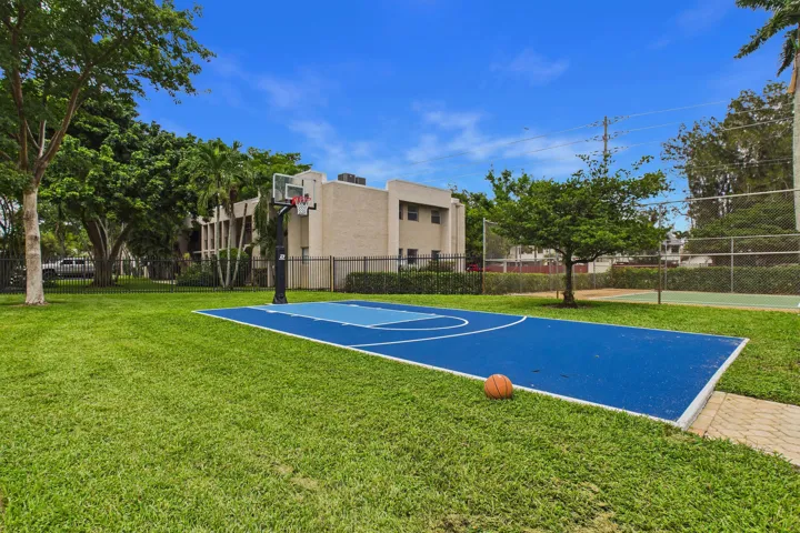 Outdoor basketball court with a blue surface, surrounded by green lawn and mature trees