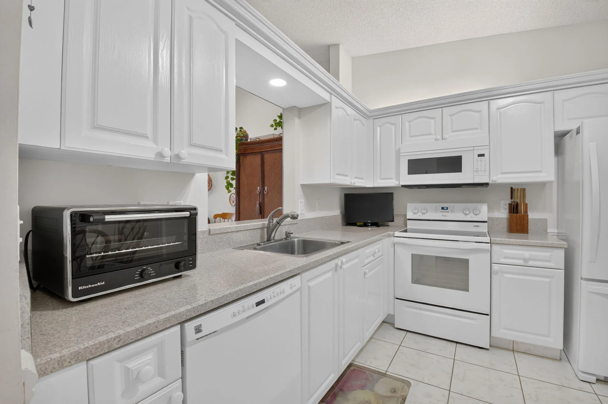 White cabinetry, light-toned countertops, tile flooring, built-in microwave, and electric range