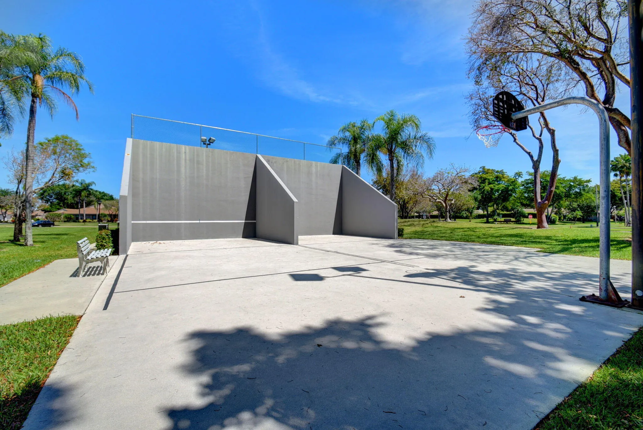 Concrete court with a basketball hoop, adjacent to a gray wall featuring safety netting
