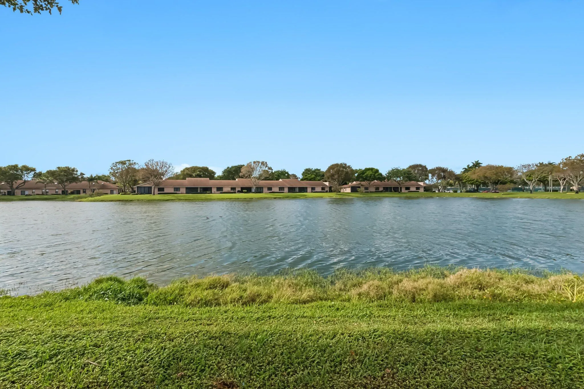 Expansive waterfront property featuring a large lake, surrounding greenery, and a clear sky
