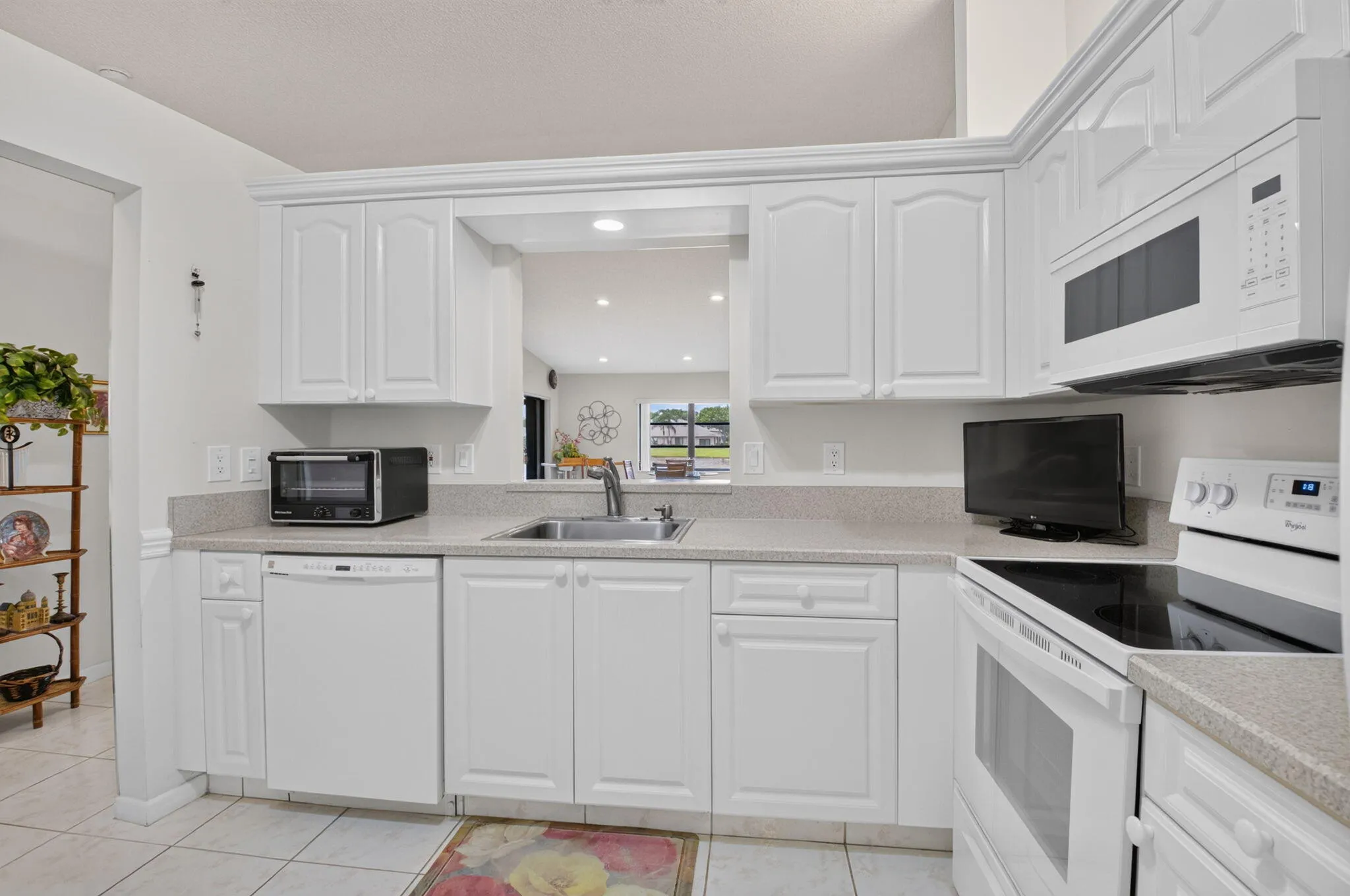 Bright, open kitchen featuring white cabinetry with raised-panel doors, stainless steel appliances including double wall ovens, granite countertops, undermount sink with chrome fixtures, and tile flooring