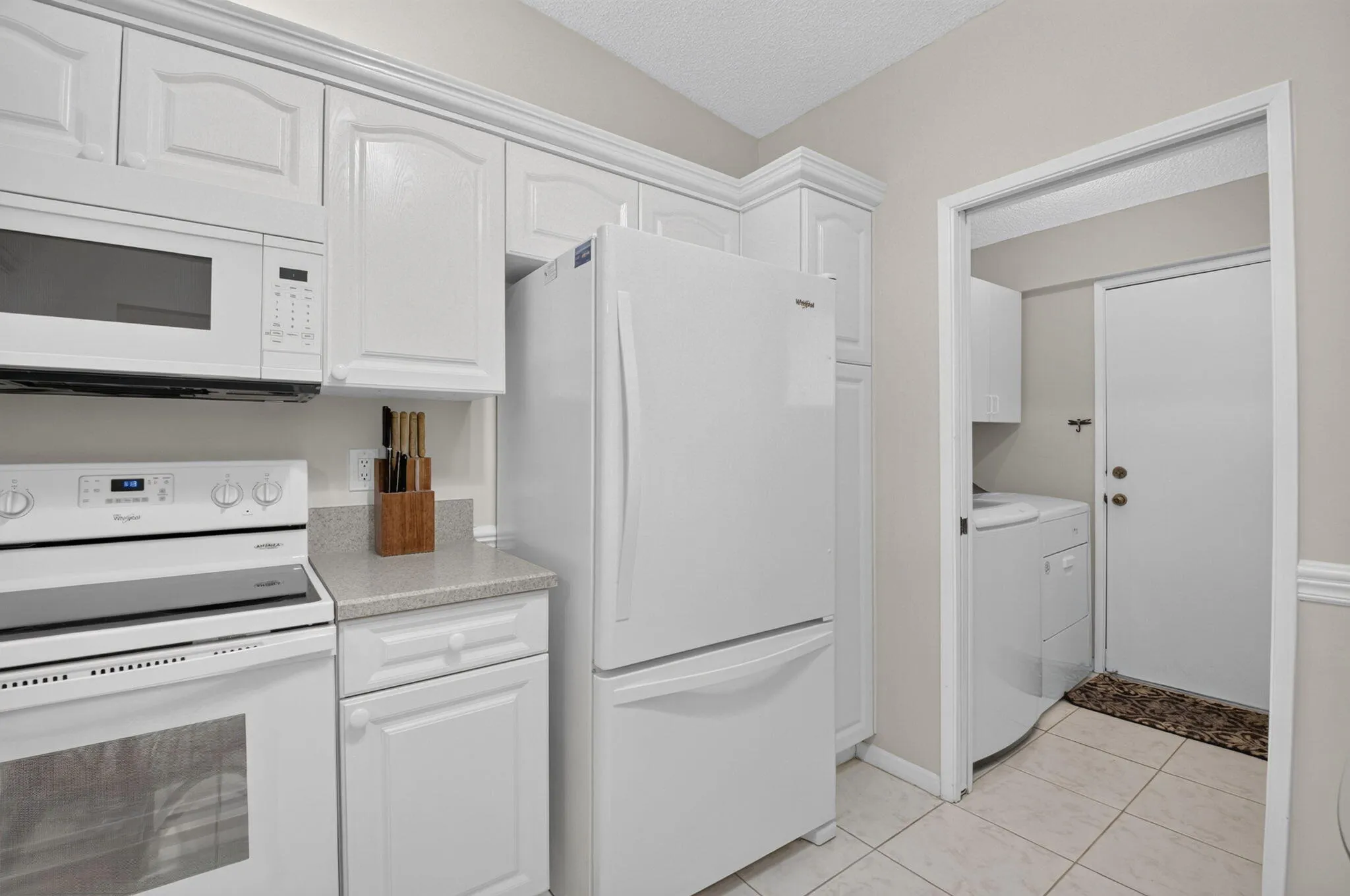 White kitchen cabinetry, white refrigerator, white range, white microwave, and light-toned countertops