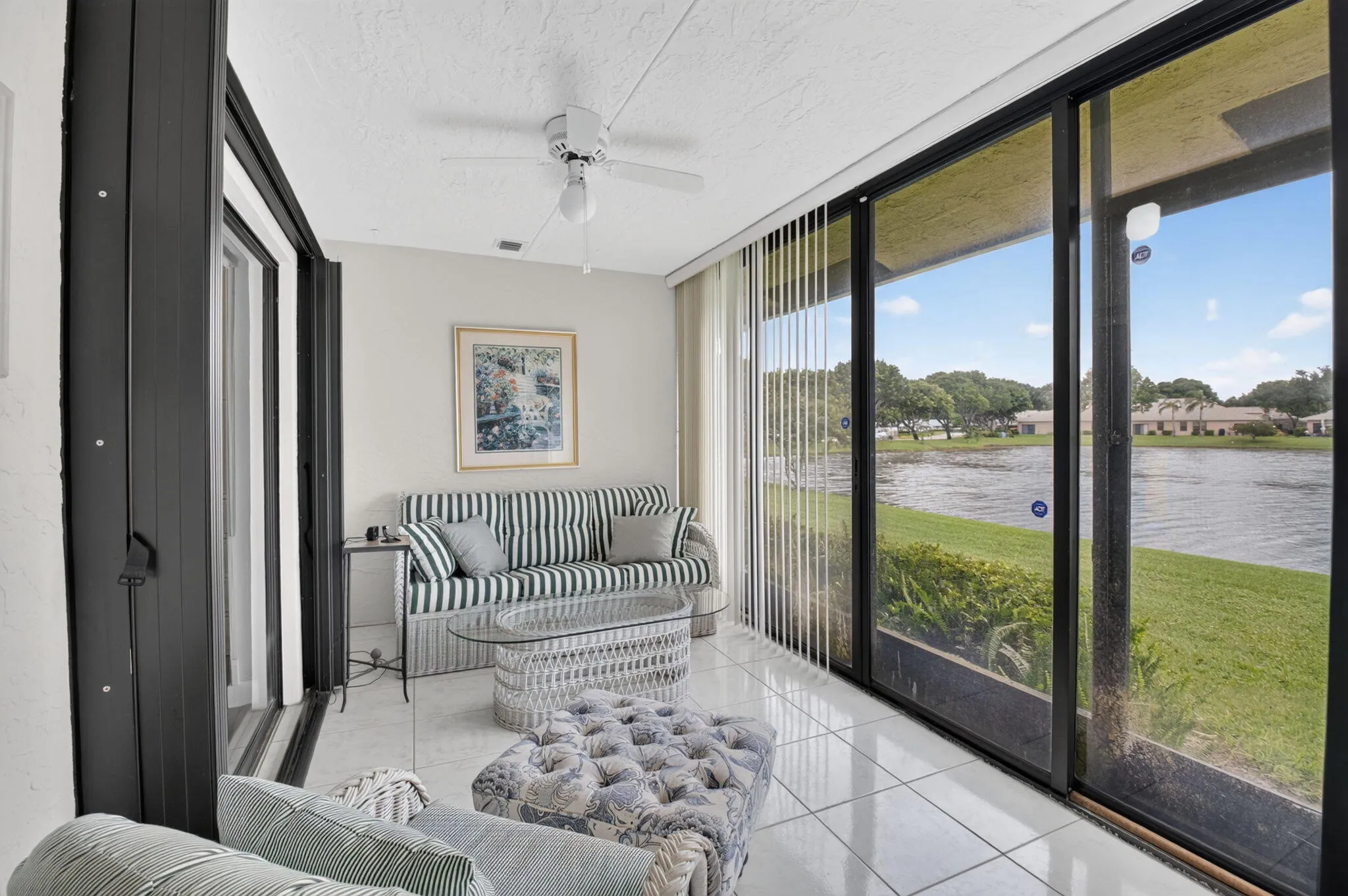 Glassed enclosed patio--with direct water frontage, featuring full-height sliding glass doors, white tiled flooring, and a ceiling fan