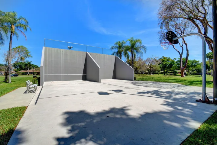 Concrete court with a basketball hoop, adjacent to a gray wall featuring safety netting