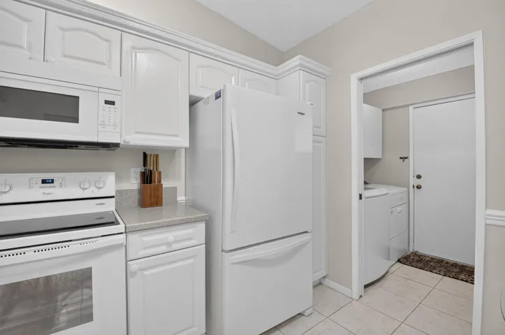 White kitchen cabinetry, white refrigerator, white range, white microwave, and light-toned countertops