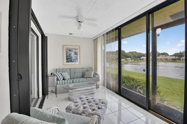 Glassed enclosed patio--with direct water frontage, featuring full-height sliding glass doors, white tiled flooring, and a ceiling fan