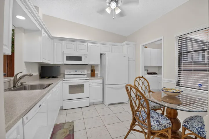 Kitchen featuring white cabinetry, white appliances, a stainless steel sink, light-toned countertops, and tiled flooring
