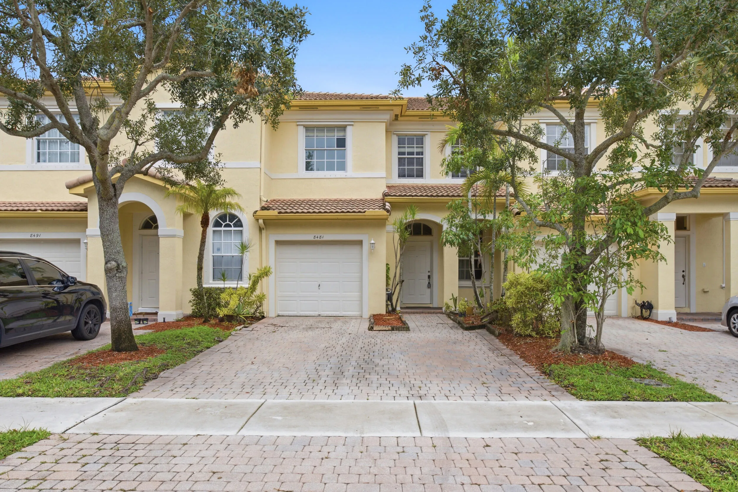 Two-story stucco facade featuring an arched entryway, white-framed windows, and an attached garage