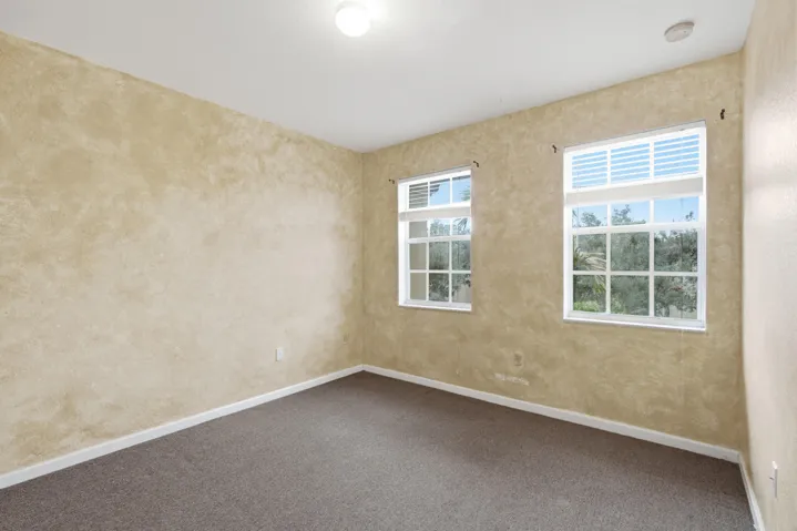 Neutral-toned walls with a textured finish, two windows featuring white blinds, and carpeted flooring