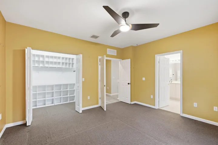 Spacious room featuring carpeting, a ceiling fan with integrated lighting, and a built-in closet with shelving and storage cubbies