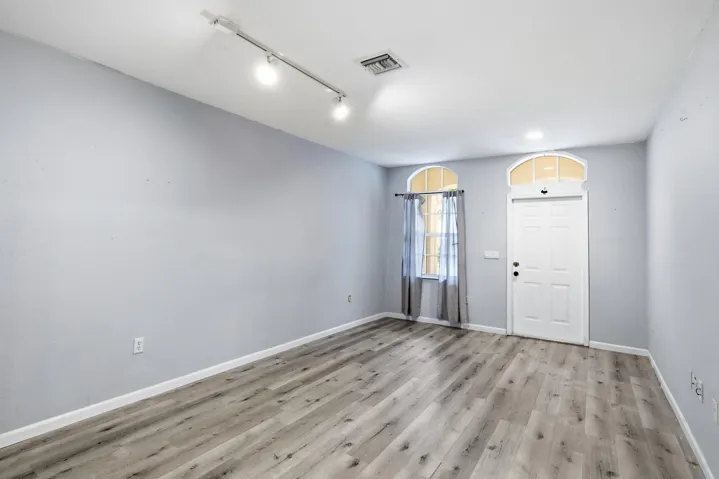 Wood-finish flooring, track lighting, arched transom window, and a paneled entry door