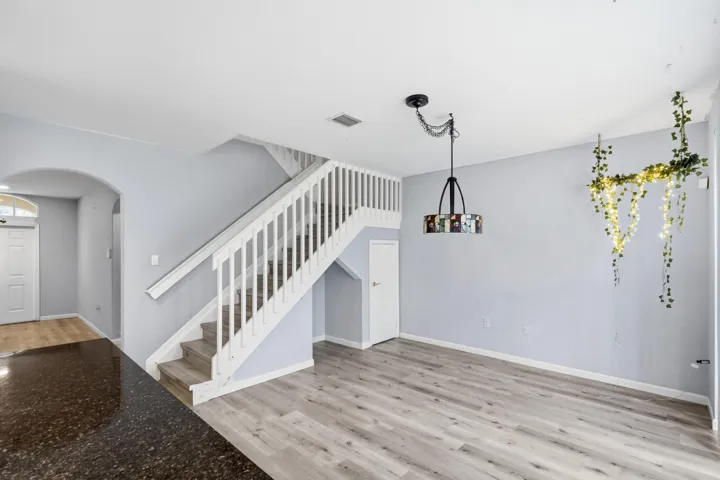 Wood-finish flooring, white staircase with balusters, dark speckled countertop, and a decorative pendant light fixture