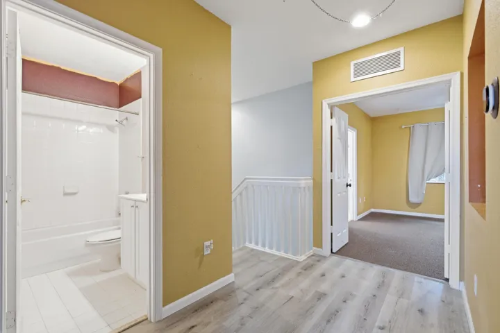 Wood-finish flooring throughout, white balustrade, interior window, and built-in bathroom cabinetry