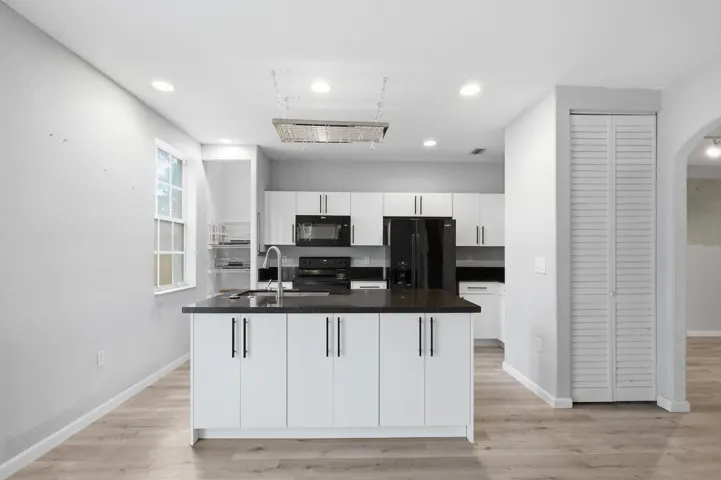Kitchen featuring an island, black countertop, white cabinetry, recessed lighting, and wood-finish flooring