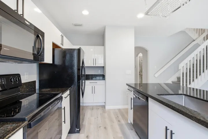 Modern kitchen featuring white cabinetry, dark countertops, wood-finish flooring, and black appliances