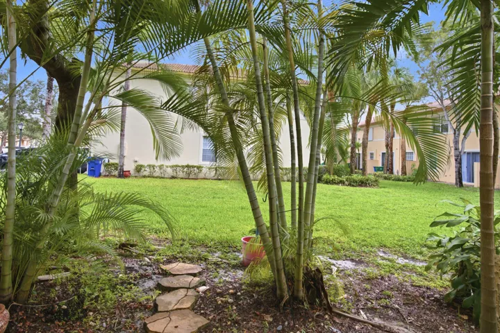 Lush landscaping with mature palm trees, flagstone pathway, manicured lawn, and stucco exterior architecture