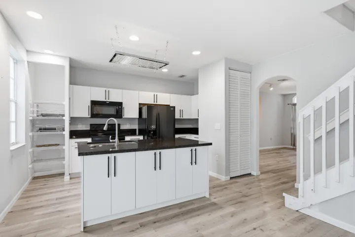 Modern kitchen featuring white cabinetry, black appliances, a central island with a dark countertop, wood-finish flooring, and recessed lighting