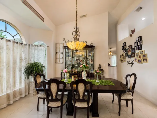 Vaulted ceiling with a decorative chandelier, arched window accents, built-in display cabinetry, and light-toned tile flooring