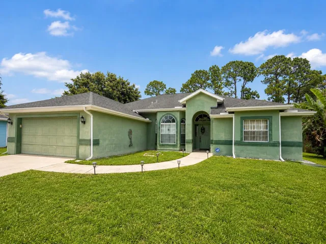 Green stucco exterior with a gray shingle roof, arched entry, curved concrete walkway, and a concrete driveway