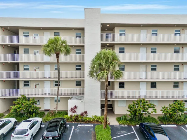 Multi-level building with individual balconies featuring white railings, surrounded by mature palm trees and established landscaping