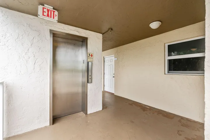 Stainless steel elevator door with call panel, textured wall finish, and overhead lighting