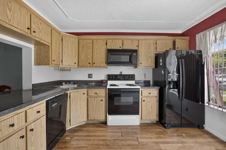 Kitchen featuring wood-finish cabinetry, dark countertops, built-in microwave, and a black refrigerator