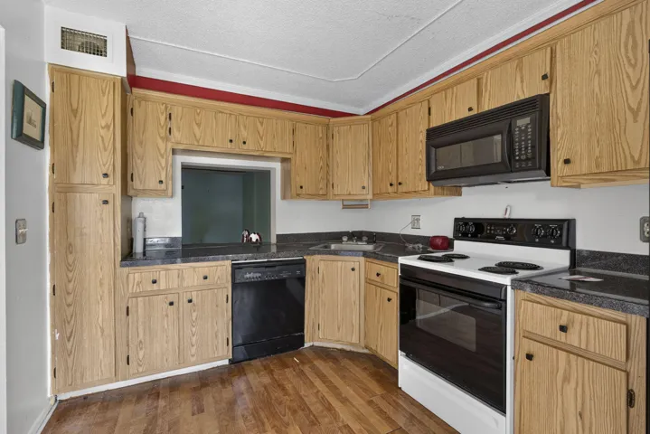 Full-height cabinetry, wood-finish flooring, built-in microwave, integrated dishwasher, and a pass-through opening