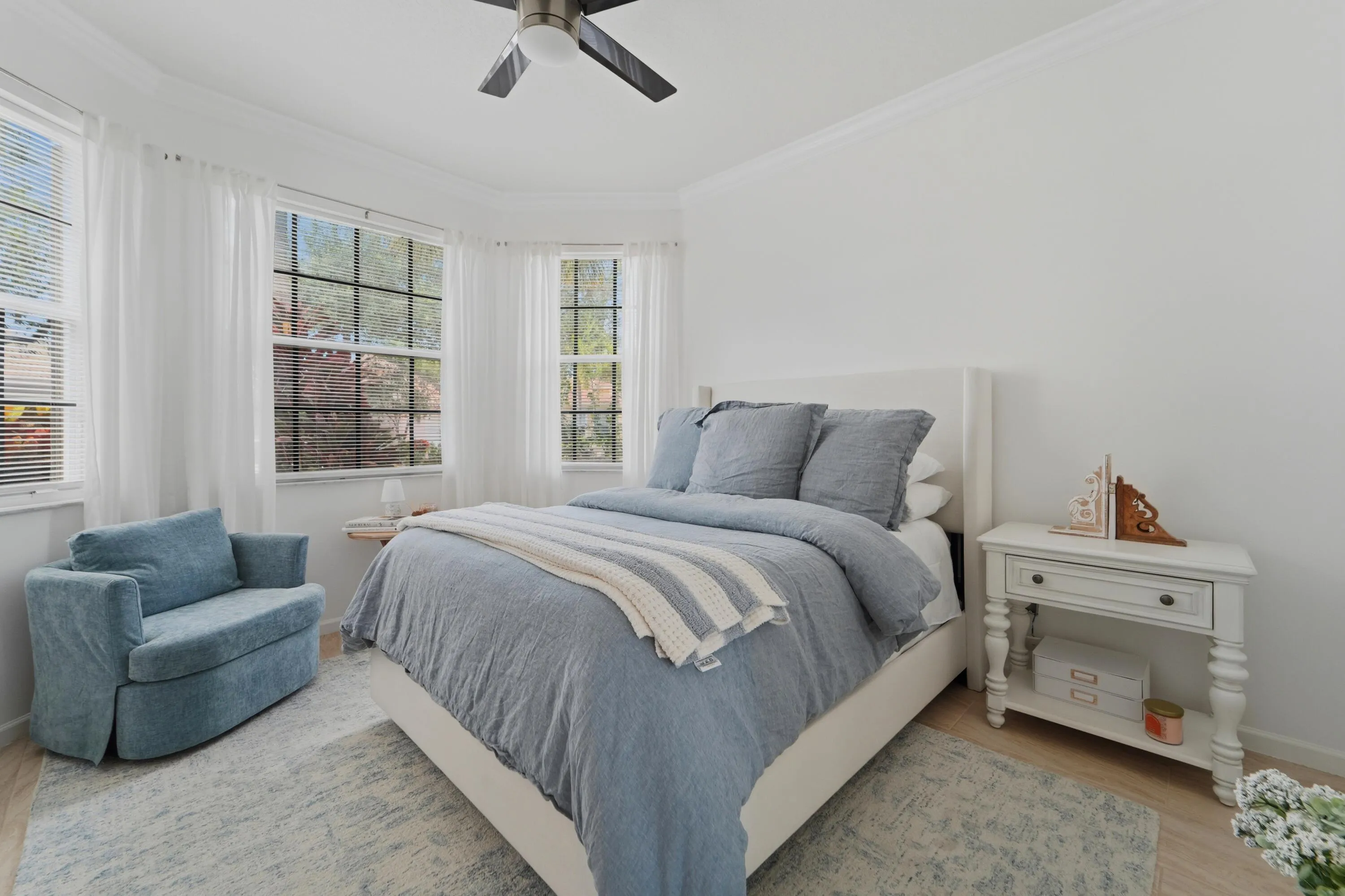 Comfortable guest bedroom features a bay window, ceiling fan and abundant natural light.
