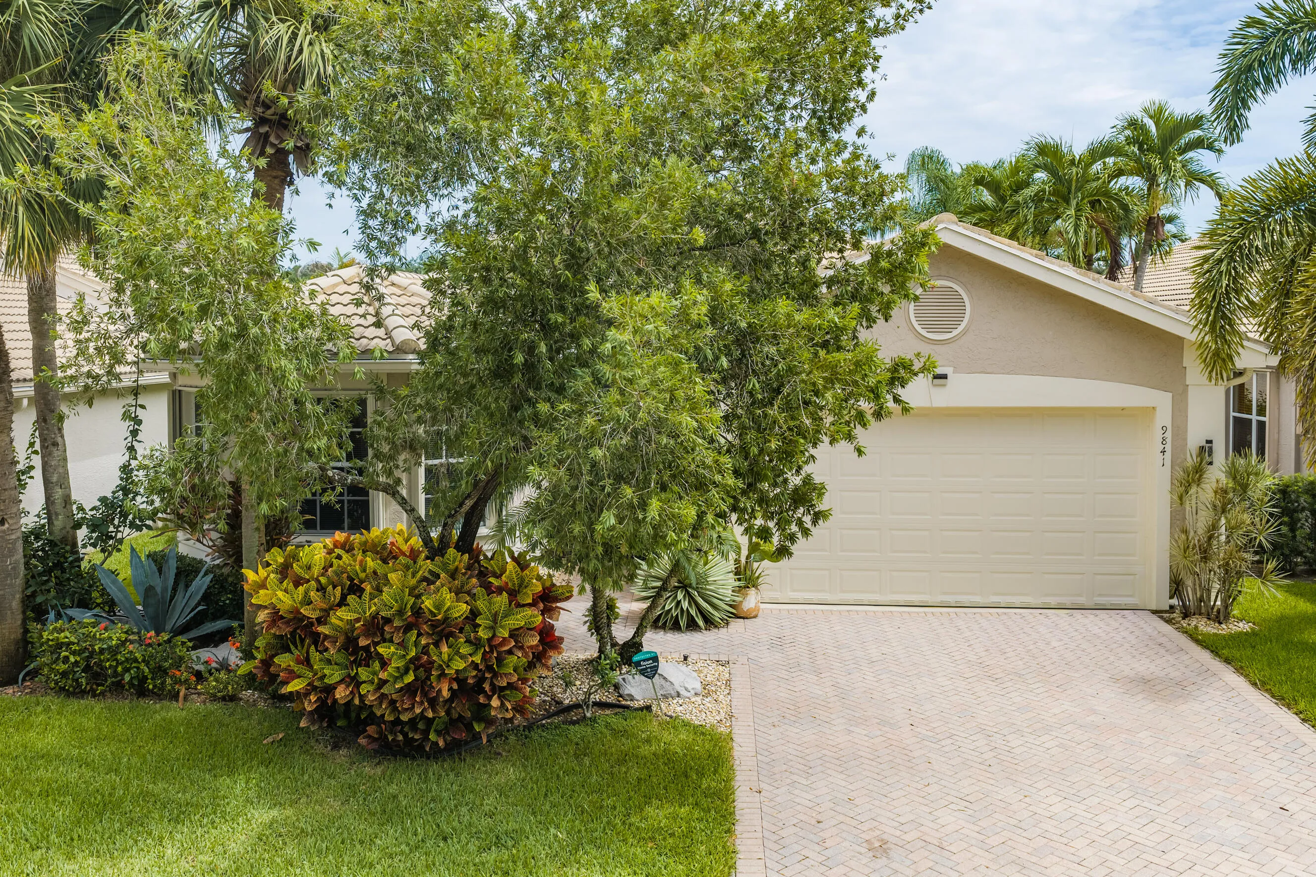 Welcoming front elevation features mature tropical landscaping, a paver driveway and attached two-car garage.