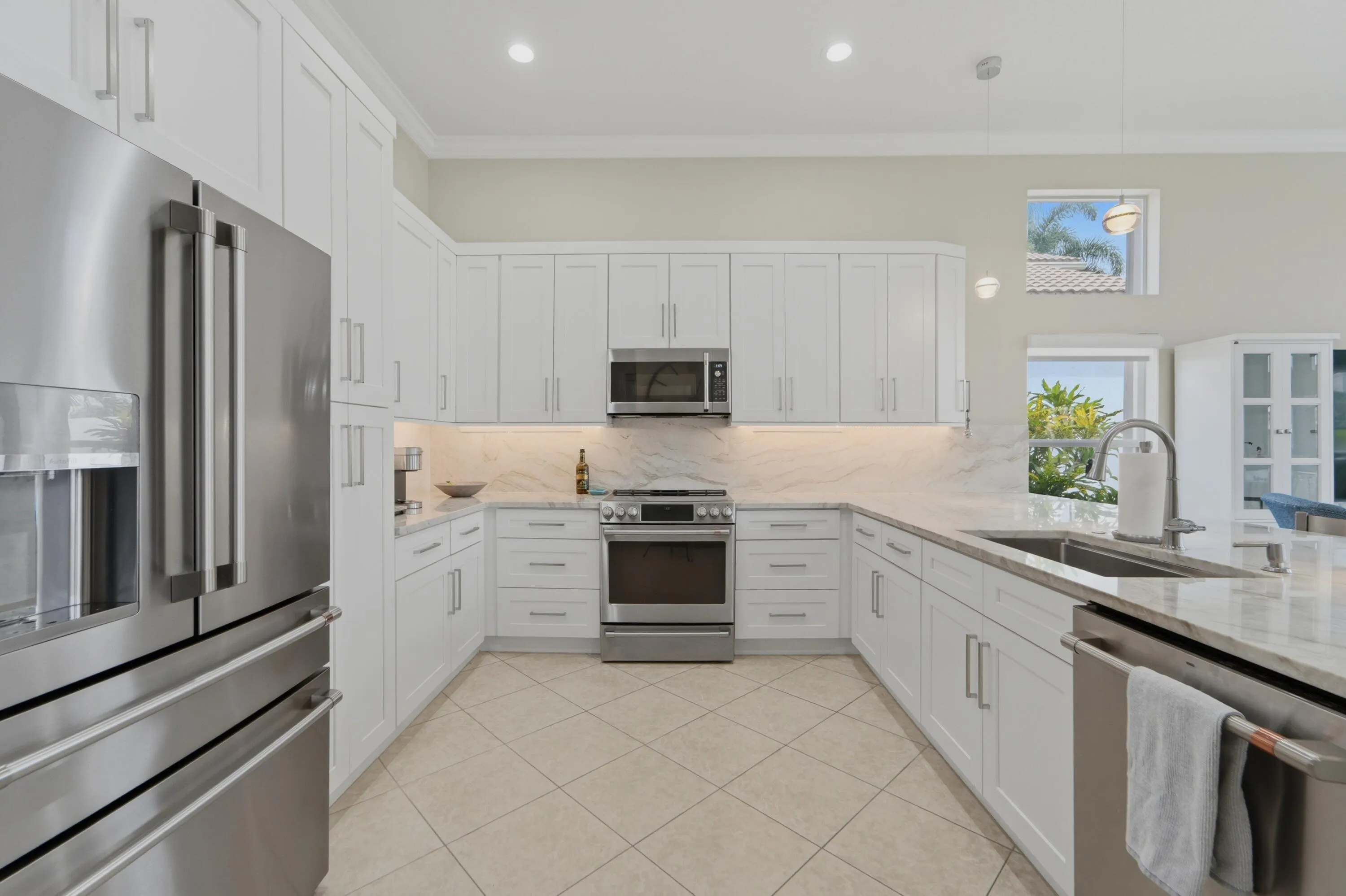 Spacious primary suite with en-suite bath and two walk in closets features a tray ceiling, natural light and French doors opening to the covered lanai.