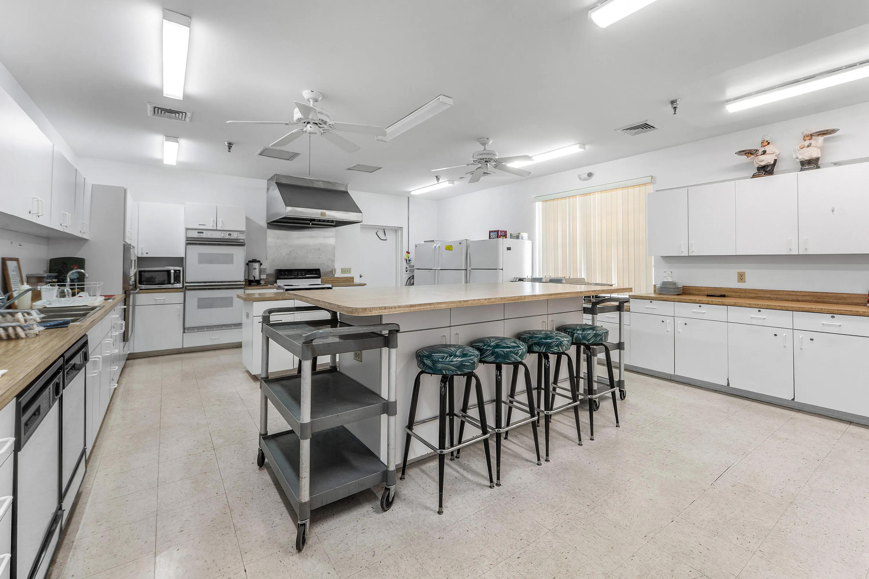Expansive kitchen with ample white cabinetry, dual ovens, multiple refrigerators, and a large center island with seating