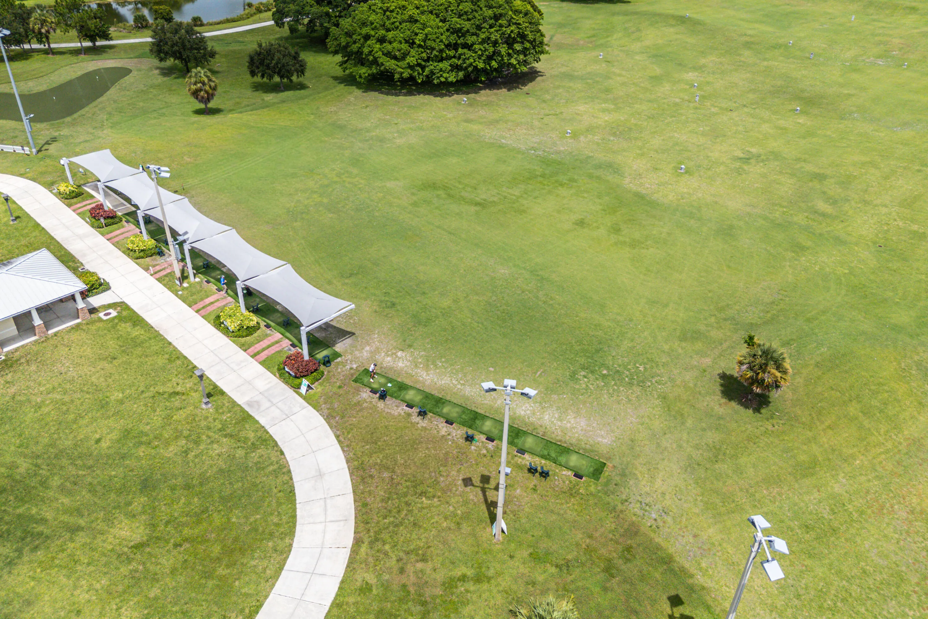Expansive green space featuring shaded structures, a walking path, and a distant water feature