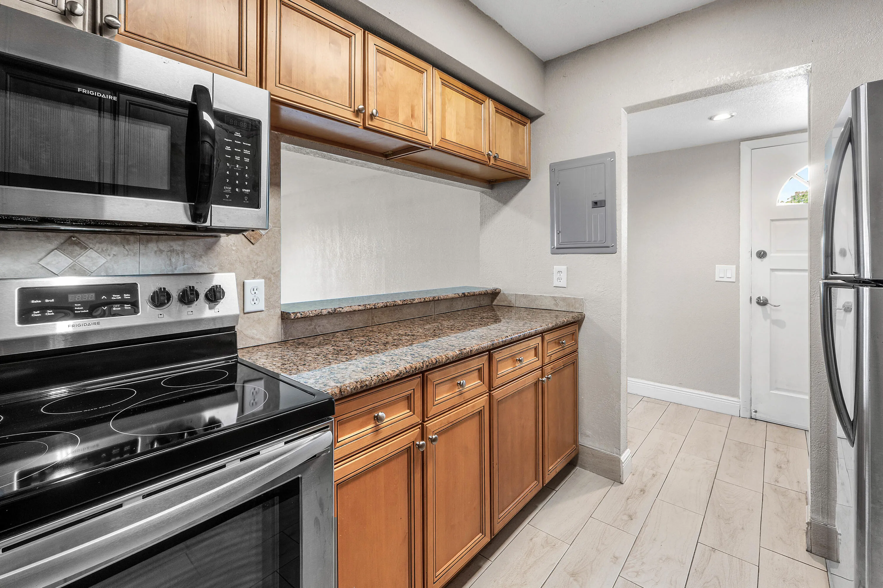 Stainless steel appliances, wood-finish cabinetry, patterned stone countertops, and light-toned tile flooring