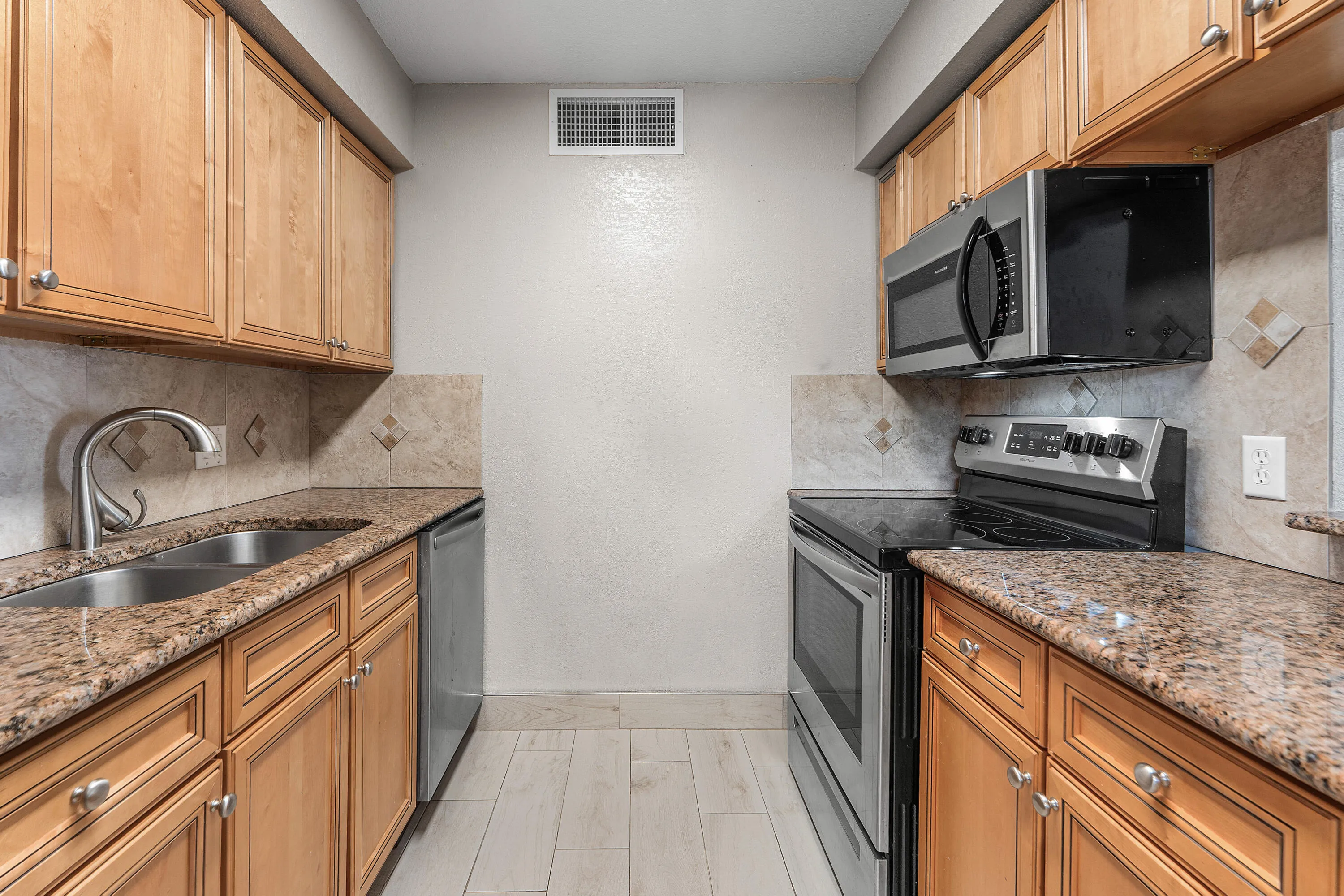 Kitchen featuring wood-finish cabinetry, stone countertops, stainless steel appliances, and a tile backsplash with accent inserts