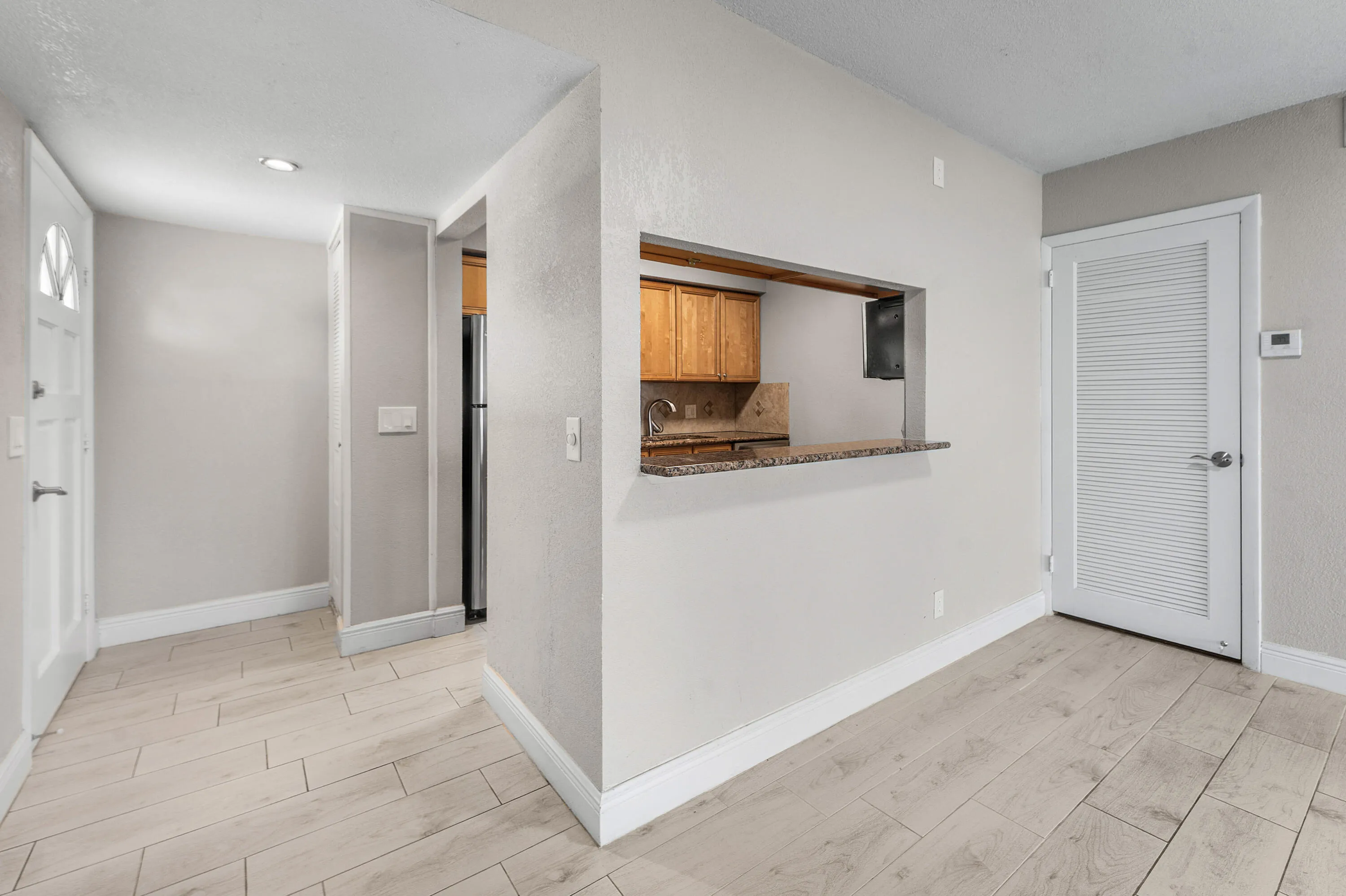 Light wood-finish flooring throughout, pass-through kitchen opening, wood cabinetry, granite counter, and recessed lighting