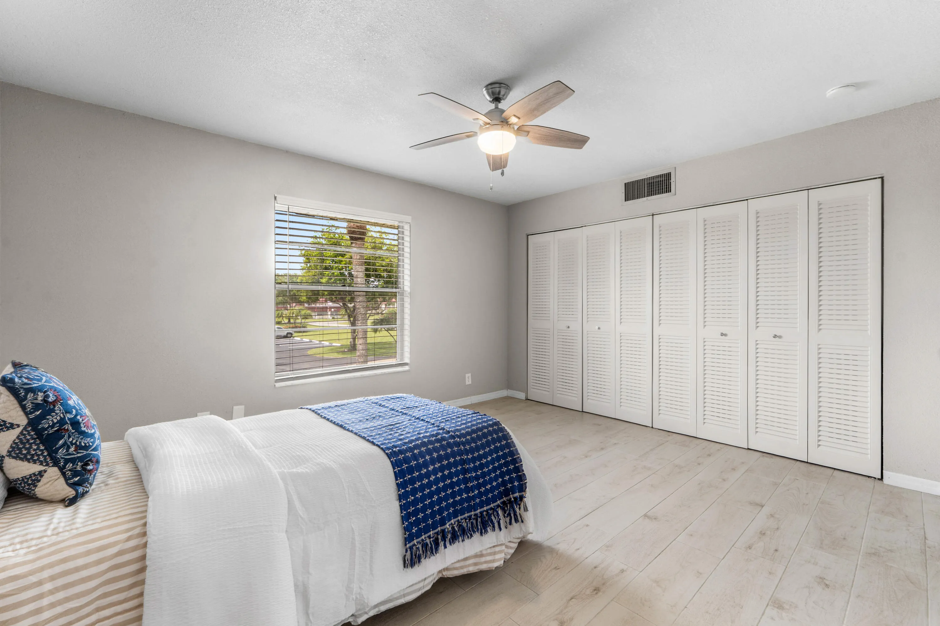 Light wood-finish flooring with white louvered bifold closet doors