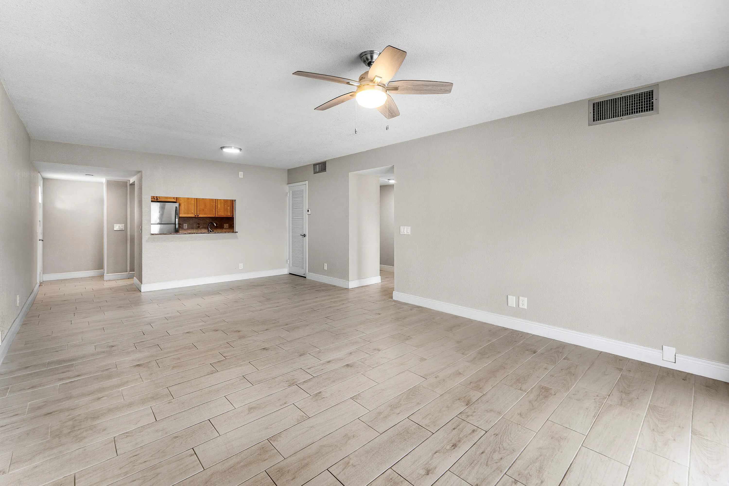Light wood-finish flooring, ceiling fan with integrated lighting, recessed lighting, pass-through window with wood cabinetry, and stainless steel appliances