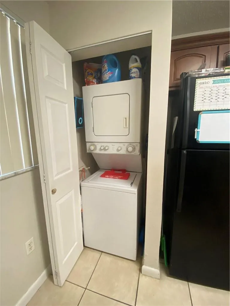 Built-in laundry closet with a stacked washer and dryer unit, white bi-fold door, and light-toned tile flooring