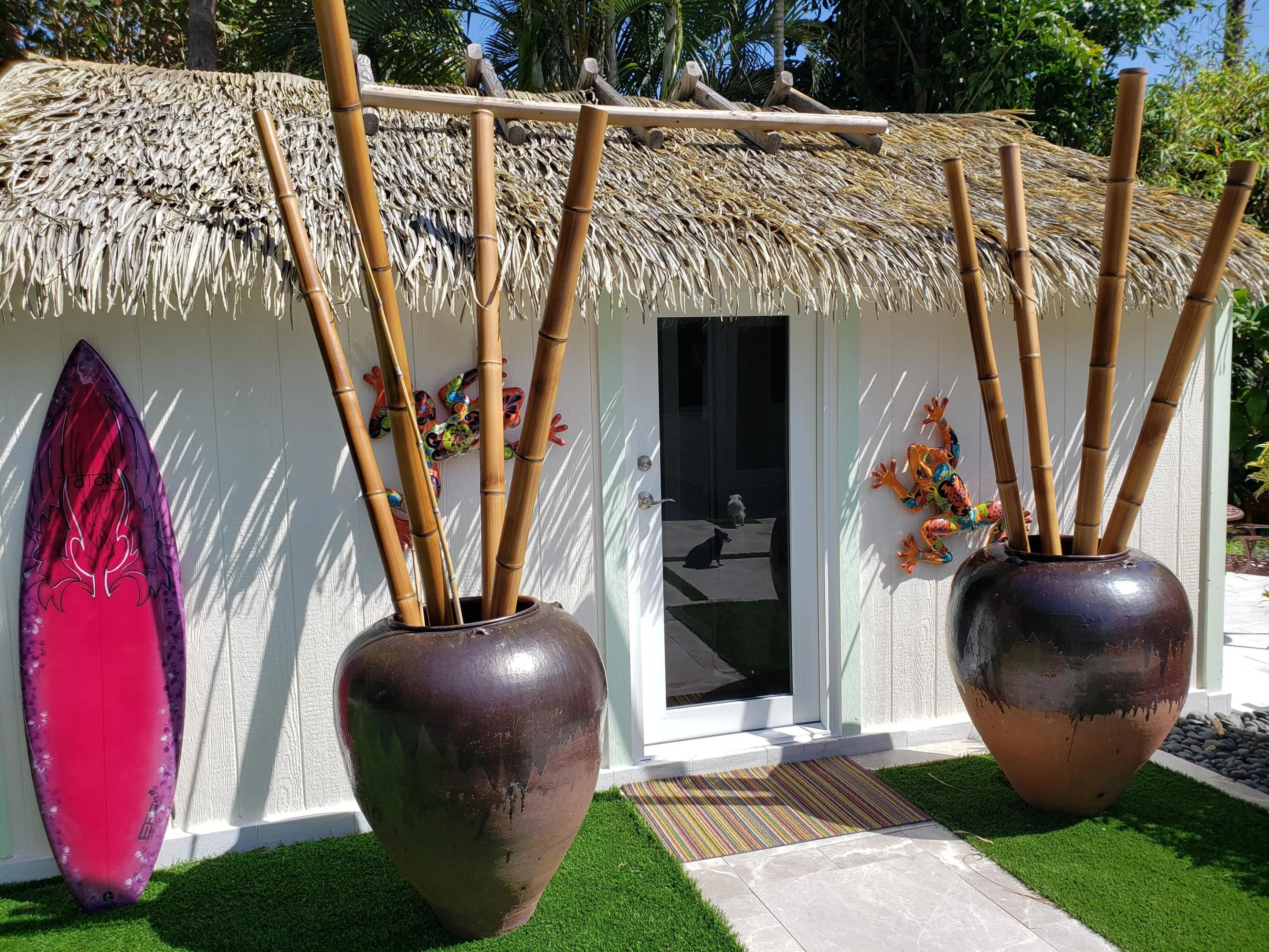 Guest Art Studio- Thatch roof efficiency featuring a glass-paneled door, decorative wall art, and artificial turf landscaping