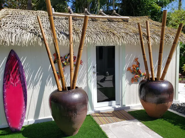 Guest Art Studio- Thatch roof efficiency featuring a glass-paneled door, decorative wall art, and artificial turf landscaping