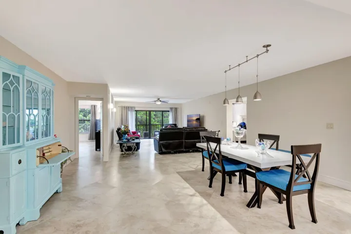 Spacious open-concept living area featuring a dining space with track pendant lighting, tile flooring throughout, and a living room with exterior balcony access
